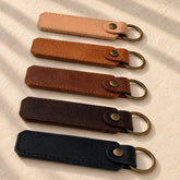 Five slim leather keyrings with brass split rings on ivory linen